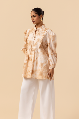 Side view of a woman wears a vibrant caramel tie-dye shirt dress with puffed sleeves, paired with white wide-leg trousers and stylish sandals.