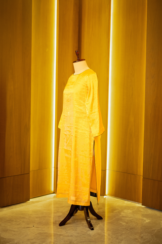 left side view of golden yellow kurta with a subtle sheen,  displayed on a mannequin against a warm wooden backdrop.