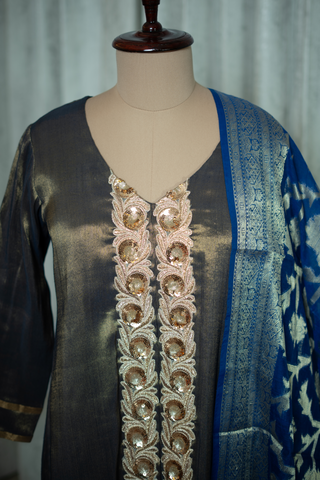 A close-up of a dark grey ethnic outfit featuring intricate gold embroidery down the front and a matching blue dupatta draped on the side.