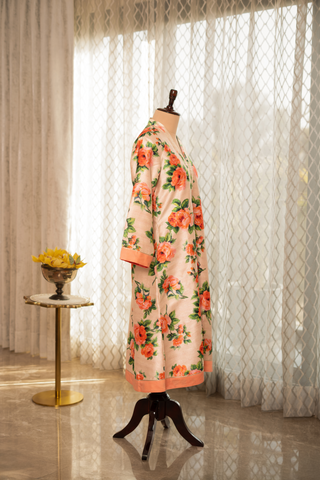 Side view of a White floral-patterned dress on a mannequin, positioned in a bright room with sheer curtains, next to a small table holding a bowl of yellow flowers.