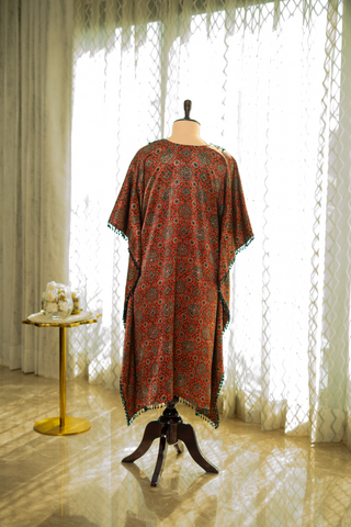 back view of red and black printed kaftan with intricate detailing and tassel edges, displayed on a mannequin against a softly lit curtain backdrop.