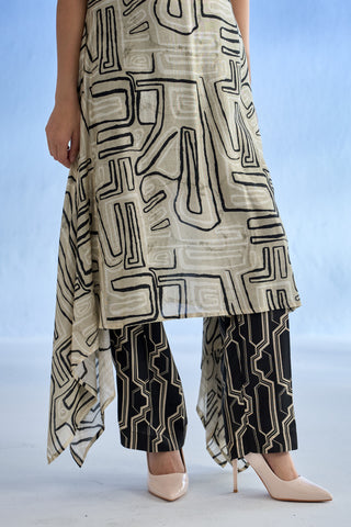 A model wearing a beige and black geometric patterned linen co-ord set with matching patterned wide-leg pants and nude heels, shown from the waist down against a light blue studio backdrop.