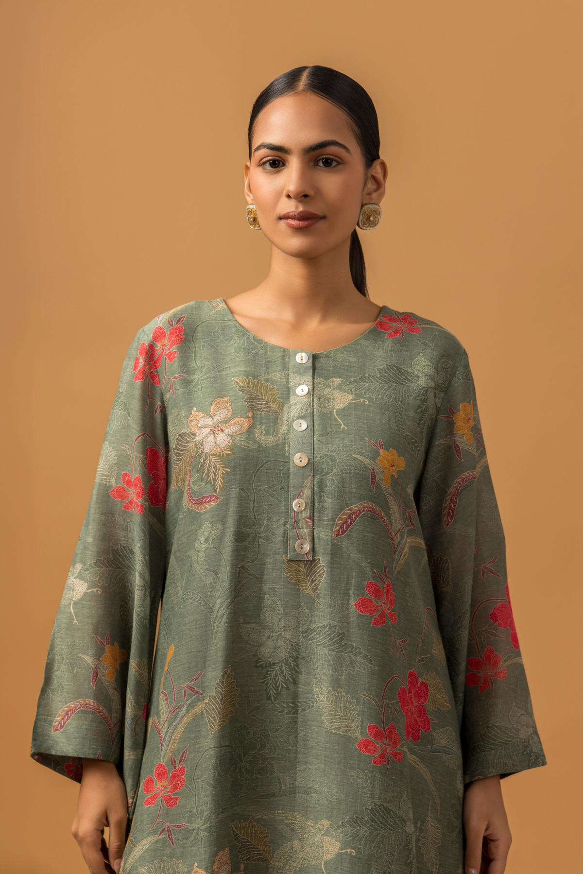 Closeup view of a woman wearing a dusty green floral line co-ord set and matching pants, set against a warm, neutral background.