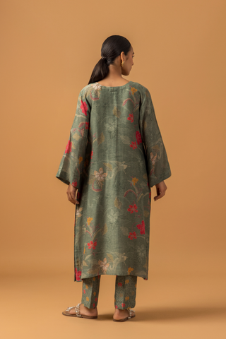 Back view of a woman wearing a dusty green floral line co-ord set and matching pants, set against a warm, neutral background.