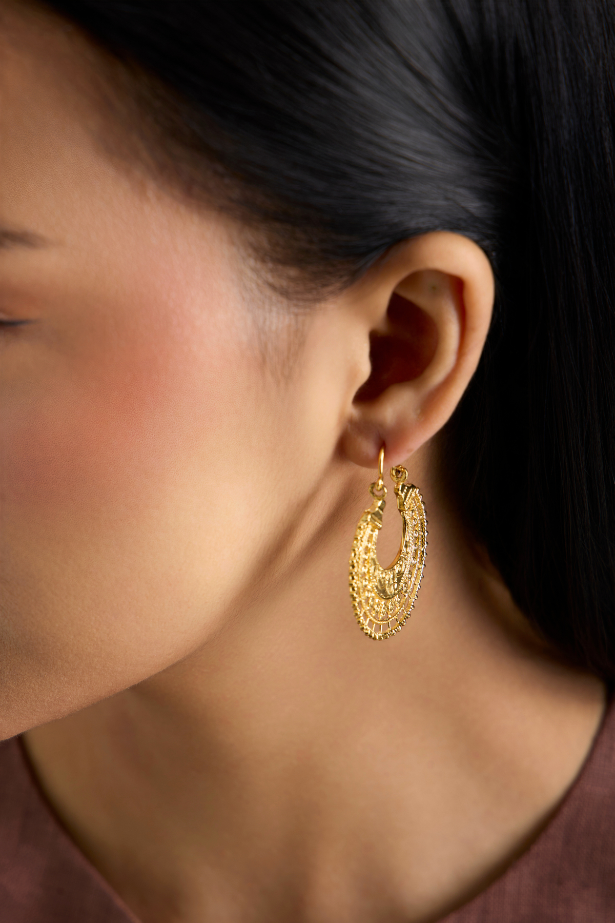 A close-up side profile of a woman wearing a textured gold crescent-shaped hoop earring.