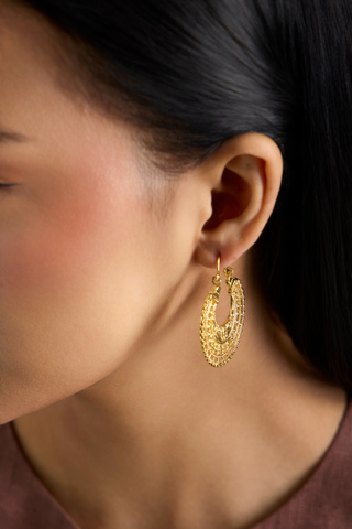 A close-up side profile of a woman wearing a textured gold crescent-shaped hoop earring.