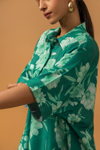 Closeup view of a woman showing her hand & wearing in a vibrant green floral co-ord set, featuring a loose shirt and matching pants, complemented by embellished sandals.