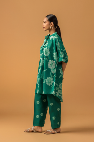 Side view of a model poses in a vibrant green floral co-ord set, featuring a loose shirt and matching pants, complemented by embellished sandals.