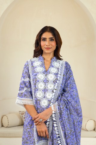Closeup View of a woman wearing a purple traditional outfit with intricate white embroidery and lace detailing, paired with matching pants, standing in front of an arched alcove in a neutral-toned interior.