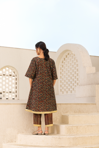 Back View of a model showcasing a brown floral printed kurta set with gold accents, paired with striped trousers, styled against an elegant outdoor backdrop.