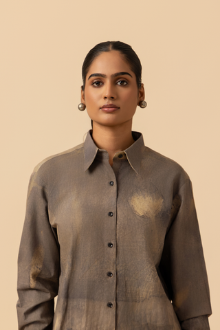 Closeup view of a model stands against a light beige background, wearing a patterned grey co-ord set which has button-up shirt and wide-legged beige pants, accessorized with heels.