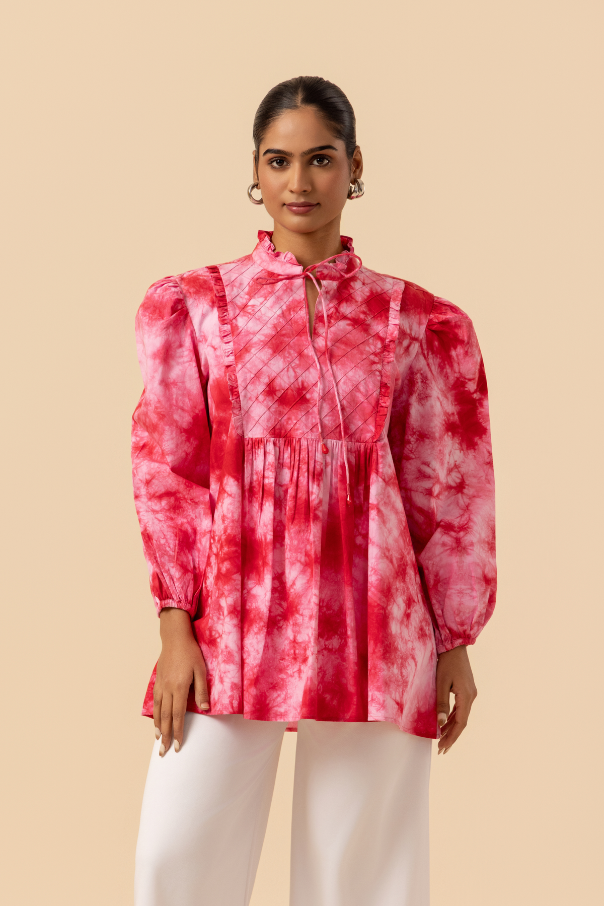 Closeup view of a model wears a vibrant cherry red tie-dye shirt dress with puffed sleeves, paired with white wide-leg trousers and stylish sandals.