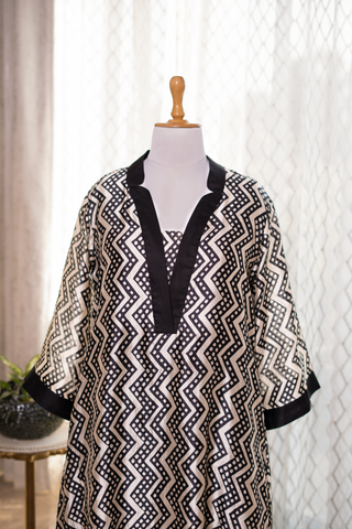 Closeup view of a black and white patterned tunic with a v-neck and wide sleeves, displayed on a mannequin against a light backdrop.