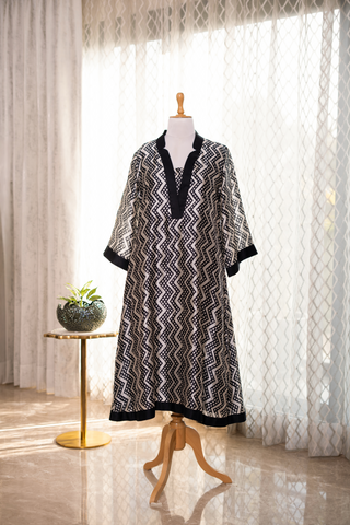 A black and white patterned tunic with a v-neck and wide sleeves, displayed on a mannequin against a light backdrop.