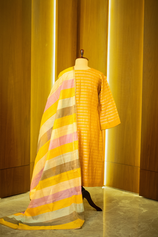 Back view of mustard yellow kurta with subtle stripes, paired with a multicolored striped dupatta, displayed on a mannequin against a warm wooden backdrop.
