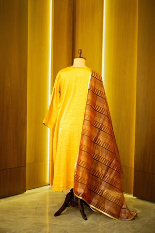 back view of golden yellow kurta with a subtle sheen, paired with a rich brown and gold woven dupatta, displayed on a mannequin against a warm wooden backdrop.