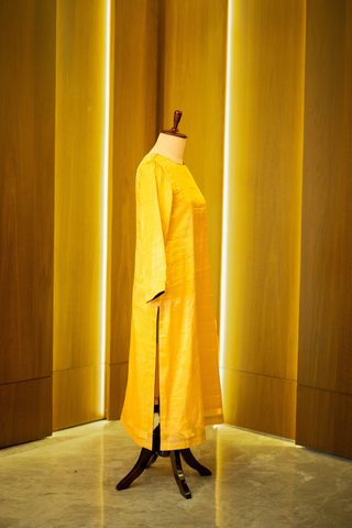 right side view of golden yellow kurta with a subtle sheen,  displayed on a mannequin against a warm wooden backdrop.
