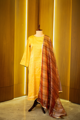 Golden yellow kurta with a subtle sheen, paired with a rich brown and gold woven dupatta, displayed on a mannequin against a warm wooden backdrop.