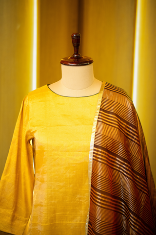 closeup view of golden yellow kurta with a subtle sheen, paired with a rich brown and gold woven dupatta, displayed on a mannequin against a warm wooden backdrop.