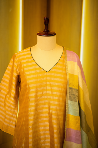 Closeup view of mustard yellow kurta with subtle stripes, paired with a multicolored striped dupatta, displayed on a mannequin against a warm wooden backdrop.