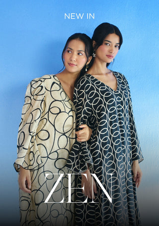 Two women modeling long flowing co-ord set dresses against a blue gradient background. The woman on the left wears a cream dress with a black abstract line pattern, and the woman on the right wears a dark charcoal dress with a white circular interlocking pattern.