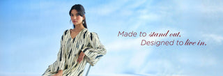 A woman wearing a loose, long-sleeve striped top in black, white, and beige, posed against a bright blue sky background with the text 'Made to stand out. Designed to live in.