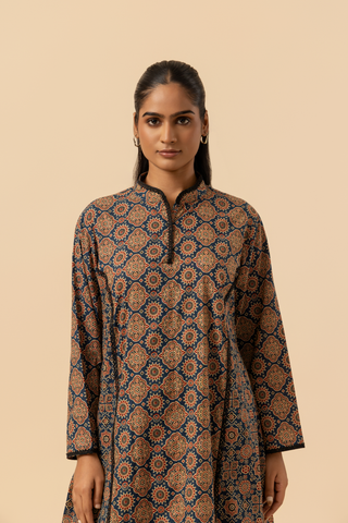 Closeup view of a woman wearing a patterned ajrakh print farshi co-ord set which has tunic with matching trousers, showcasing vibrant colors and intricate designs against a simple beige background.