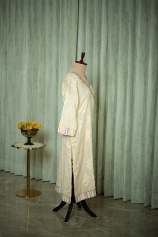 side view of white ivory embroidered kurta with subtle gold detailing and striped trim, displayed on a mannequin against a soft green curtain backdrop.