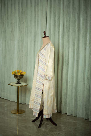 left side view of ivory embroidered kurta with subtle gold detailing and striped trim, displayed on a mannequin against a soft green curtain backdrop.