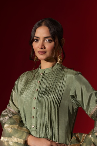 Clsoeup view of a model showcasing an elegant green gharara set with gold accents, set against a striking red background.