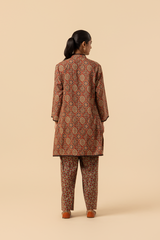 Back view of a model showcases a patterned brown ajrakh print co-ord set and against a beige background, emphasizing traditional ethnic wear.