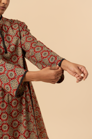 Closeup view of a model's hand wearing a red patterned ajrakh print farshi salwar & kurta, set against a soft beige background.