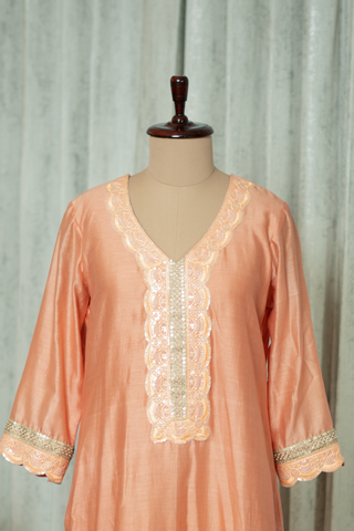 closeup view of a peach silk kurta with intricate embroidery on display, featuring elegant sleeves and neckline detailing, set against a modern backdrop.