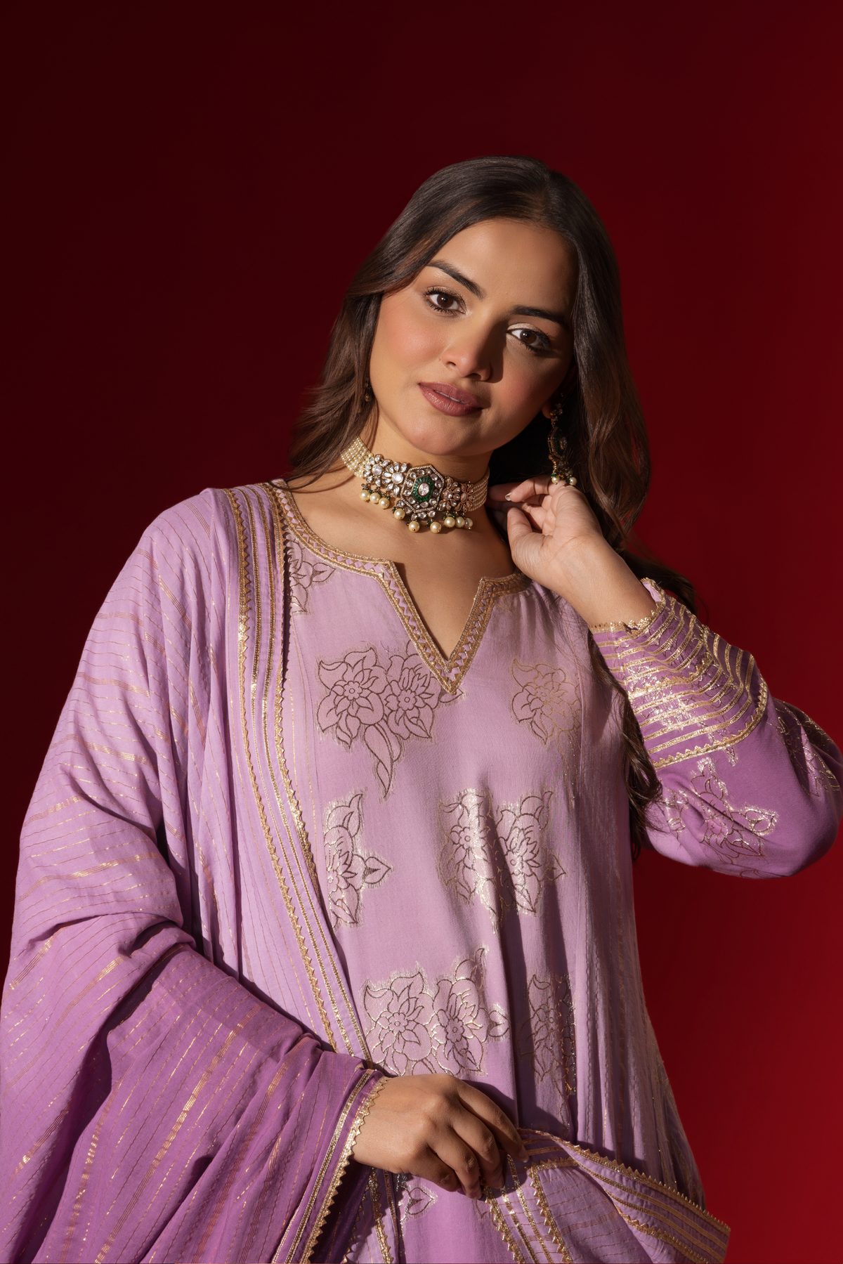 Closeup view of a woman showcases an elegant lilac anarkali kurta set with intricate designs, contrasting beautifully against a deep red background.