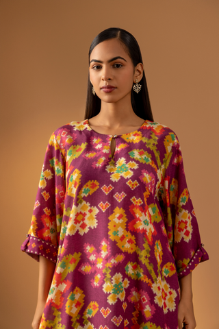 Closeup view of a model showcases a magenta floral-patterned co-ord set paired with colorful striped pants against a warm, neutral background.