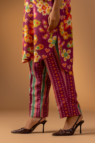 A close-up of a woman wearing a magenta floral-patterned co-ord set paired with colorful striped pants against a warm, neutral background