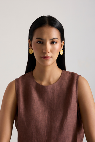 A woman with long black hair is shown from the chest up against a plain light gray background. She is wearing a sleeveless dusty rose-brown top and round gold earrings.