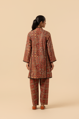 Back view of a model showcases a vibrant, patterned ethnic ajrakh printed farshi co-ord set featuring a long tunic and matching pants in rich red tones.