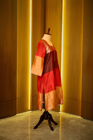 right side view of multicolored patchwork kurta in shades of red, pink, and gold, displayed on a mannequin against a warm wooden backdrop.