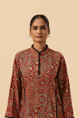 Closeup view of a model showcases a vibrant, patterned ethnic ajrakh printed farshi co-ord set featuring a long tunic and matching pants in rich red tones.