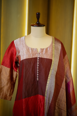 closeup view of multicolored patchwork kurta in shades of red, pink, and gold, paired with a coordinating striped dupatta, displayed on a mannequin against a warm wooden backdrop.