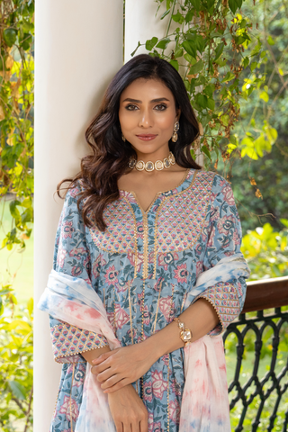 Closeup view of a woman stands elegantly in a beautiful, patterned block printed ethnic kurta set with intricate details, surrounded by lush greenery and architectural columns.