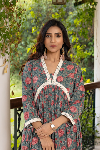 Closeup view of a woman stands elegantly on a black-and-white checkered floor, wearing a floral handblock printed cotton kurta set and white pants, surrounded by greenery. 