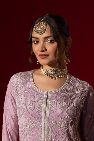 Closeup view of a woman stands confidently in a beautifully lavender embroidered kurta set, against a rich red background.
