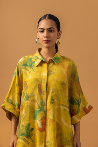 Closeup view of a model stands in a bright yellow co-ord set featuring a patterned oversized shirt and matching striped pants against a warm backdrop.