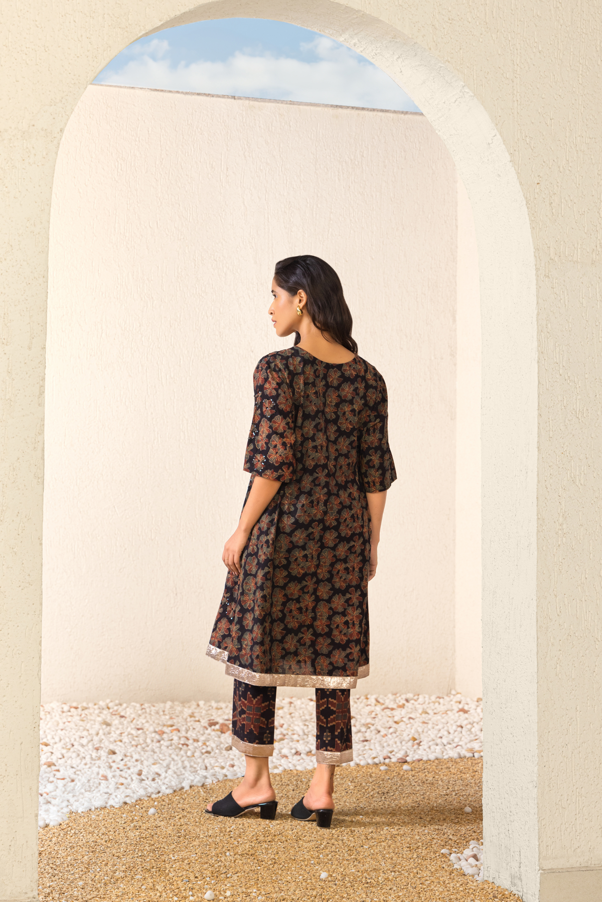 Back view of a model wearing a black floral linen kurta set with matching pants, styled in an elegant outdoor archway setting