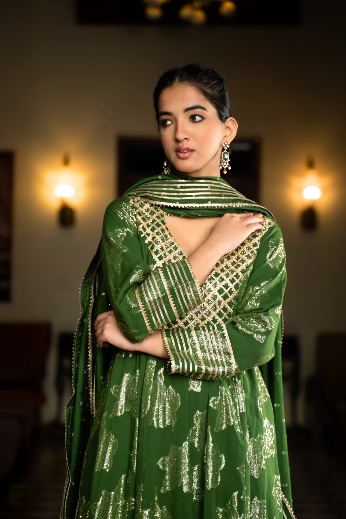 Closeup view of a woman in a vibrant green anarkali kurta set with matching pants stands gracefully in a well-decorated interior.