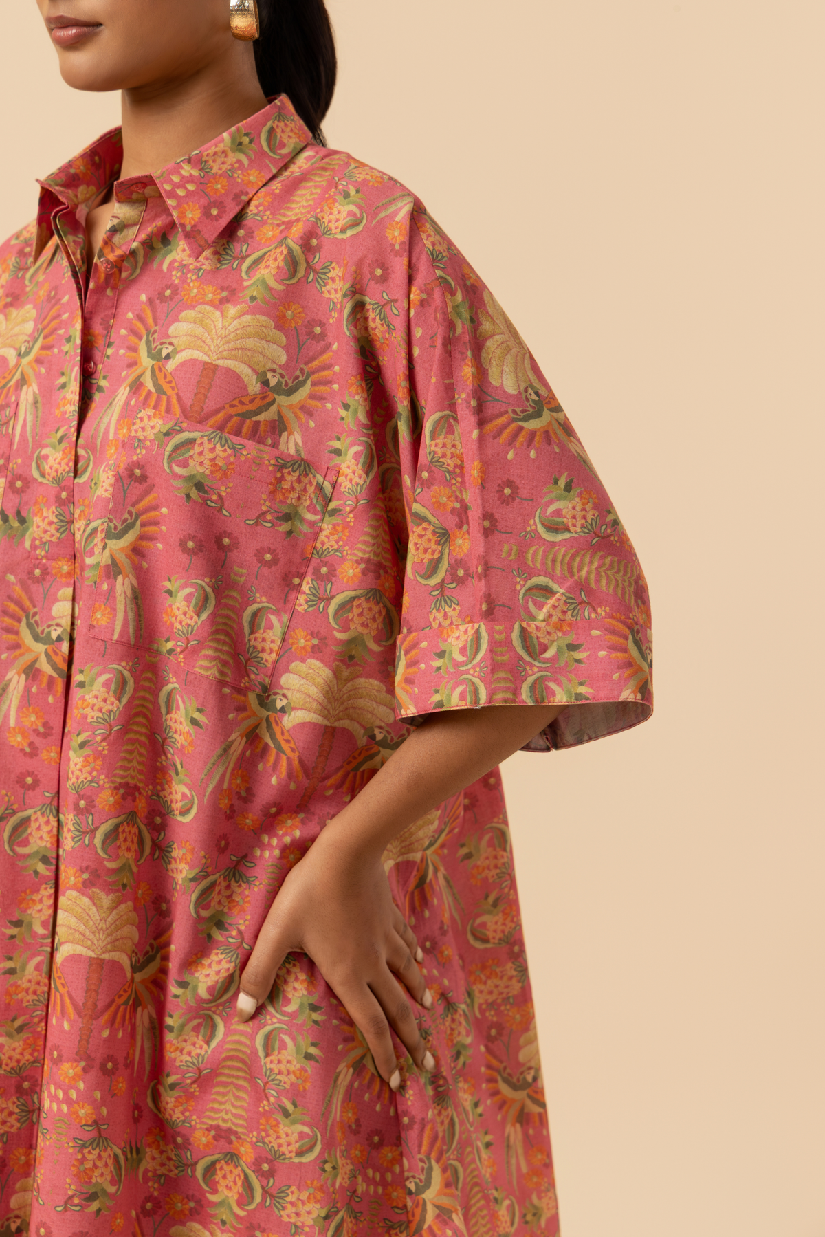 Closeup view of a woman wearing a pink patterned co-ord set shirt against a beige background