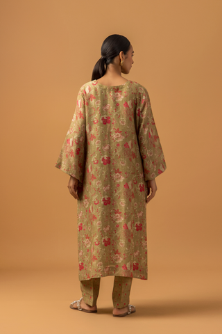 Back view of a woman in floral-patterned co-ord set with matching pants stands against a tan background, conveying a calm and elegant tone.
