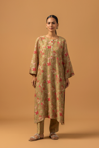 Woman in floral-patterned co-ord set with matching pants stands against a tan background, conveying a calm and elegant tone.